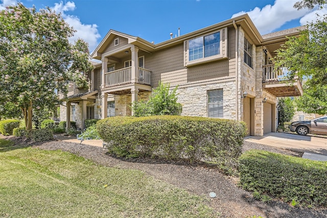 view of front of home featuring concrete driveway, an attached garage, a balcony, and stone siding