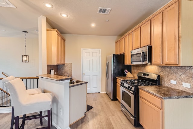 kitchen with visible vents, light brown cabinets, dark countertops, a breakfast bar, and stainless steel appliances