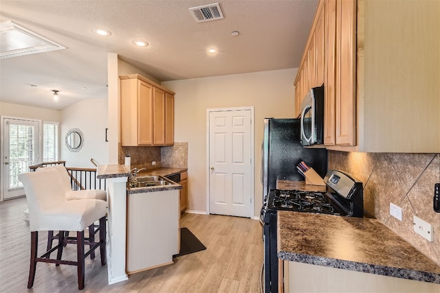 kitchen featuring visible vents, a peninsula, dark countertops, a kitchen breakfast bar, and appliances with stainless steel finishes