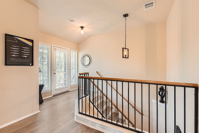 hall featuring baseboards, an upstairs landing, wood finished floors, and visible vents