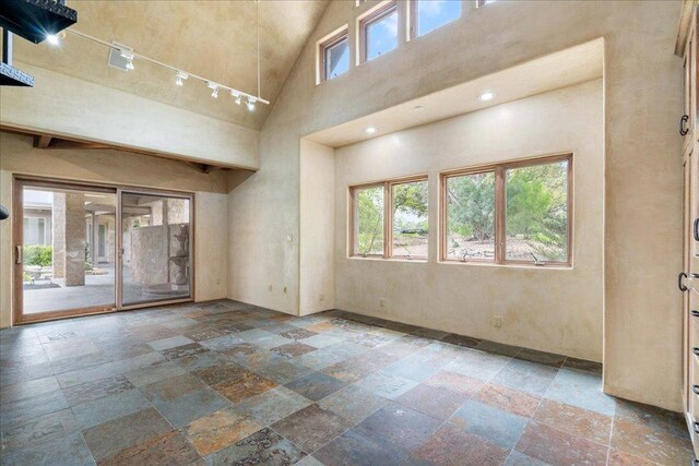 empty room with stone tile flooring, a wealth of natural light, and a high ceiling