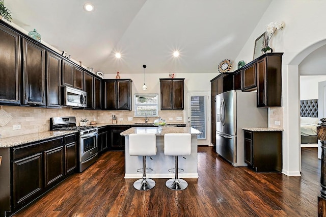 2605 Etta May Ln, Leander, TX 78641 - kitchen featuring appliances with stainless steel finishes, a kitchen island, arched walkways, dark brown cabinetry, and decorative backsplash