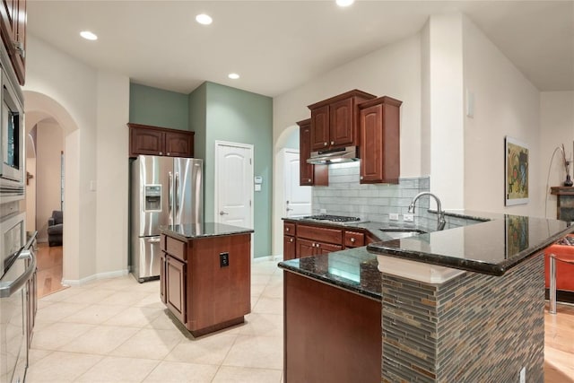 2009 Manada Trl, Cedar Park, TX 78641 - kitchen with stainless steel appliances, arched walkways, a peninsula, under cabinet range hood, and dark stone countertops