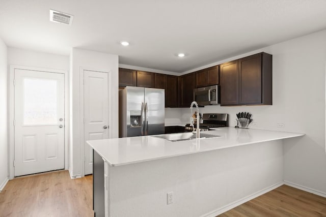 197 Buenos Aires, Kyle, TX 78640 - kitchen with appliances with stainless steel finishes, light wood-type flooring, dark brown cabinets, a peninsula, and light countertops