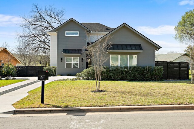 view of front of home featuring a front lawn, a standing seam roof, fence, and metal roof
