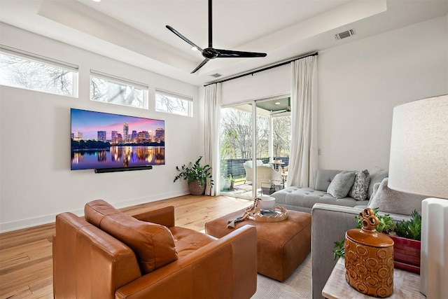living room with wood finished floors, visible vents, ceiling fan, and a tray ceiling