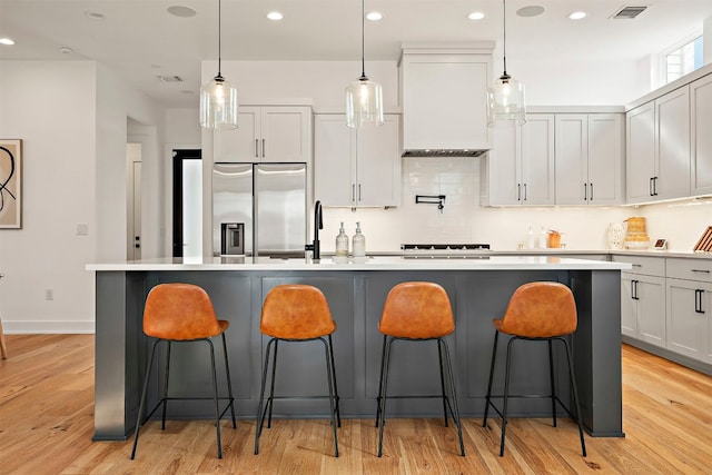 kitchen with a kitchen island with sink, light wood-style flooring, a sink, visible vents, and stainless steel fridge with ice dispenser