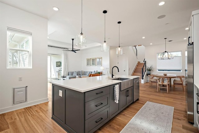 kitchen with stainless steel appliances, light countertops, gray cabinets, a sink, and a center island with sink
