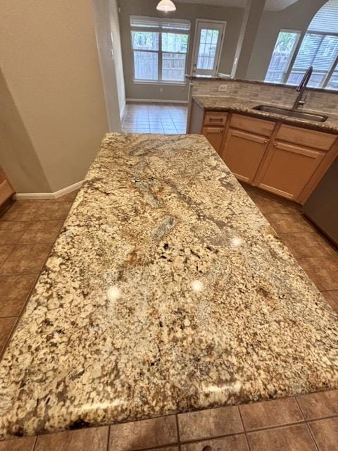 kitchen featuring baseboards, light stone counters, tile patterned flooring, and a sink