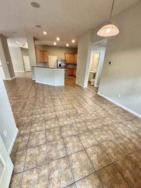 kitchen featuring brown cabinets, open floor plan, stainless steel refrigerator with ice dispenser, baseboards, and recessed lighting