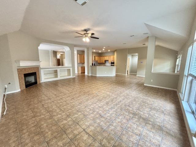 unfurnished living room featuring visible vents, baseboards, a fireplace, a ceiling fan, and vaulted ceiling
