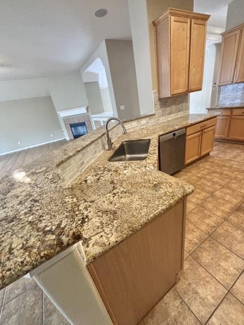 kitchen featuring tasteful backsplash, a tiled fireplace, a sink, light stone counters, and dishwasher