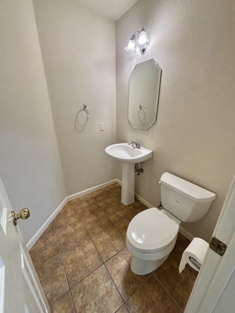 half bath with baseboards, toilet, tile patterned flooring, and a sink