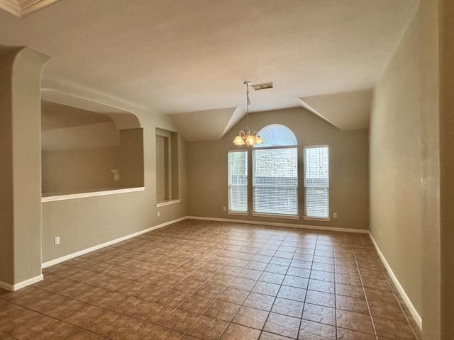 tiled empty room with baseboards, lofted ceiling, and a notable chandelier