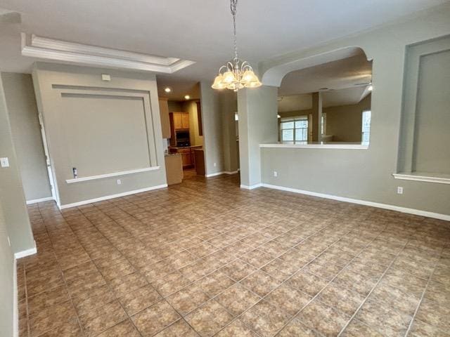 unfurnished room featuring a tray ceiling, baseboards, ornamental molding, and a chandelier