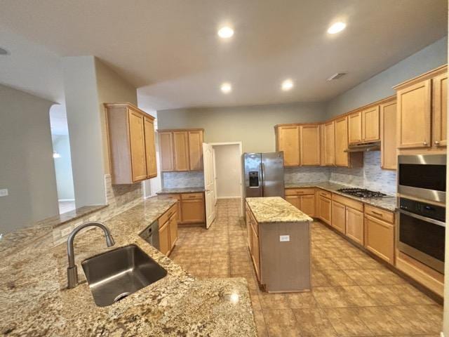 kitchen featuring light stone counters, a sink, a kitchen island, under cabinet range hood, and stainless steel appliances