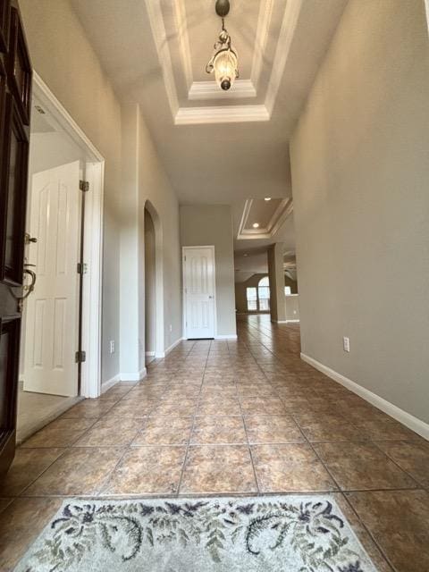 foyer entrance with a tray ceiling, tile patterned floors, baseboards, arched walkways, and ornamental molding
