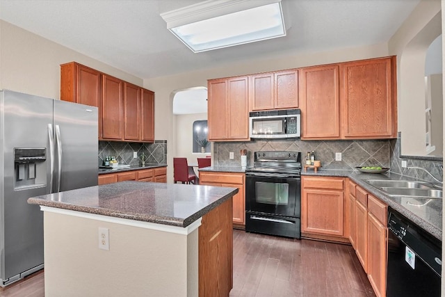 kitchen with wood finished floors, a sink, arched walkways, and black appliances