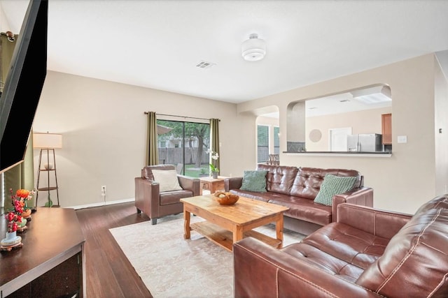 living room with arched walkways, wood finished floors, and visible vents