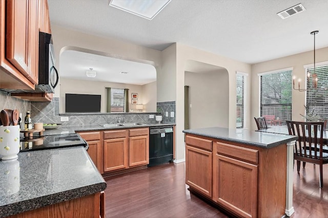 kitchen with a sink, arched walkways, stainless steel microwave, black dishwasher, and visible vents