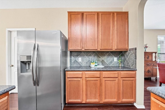 kitchen with decorative backsplash, arched walkways, stainless steel fridge, and dark wood-type flooring
