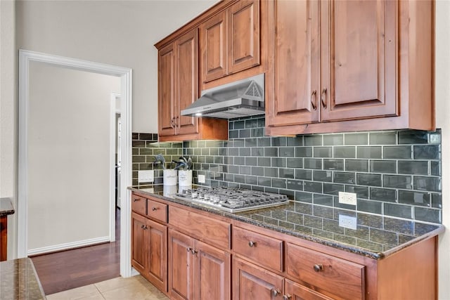 3925 Good Night Trl, Leander, TX 78641 - kitchen featuring range hood, stainless steel gas cooktop, brown cabinetry, dark stone counters, and decorative backsplash