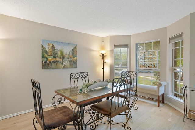 dining room featuring a textured ceiling, light wood finished floors, and baseboards