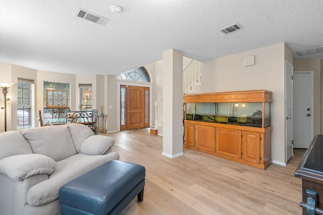 living room with a textured ceiling, visible vents, baseboards, and light wood-style floors