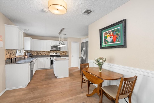 dining area with visible vents, a wainscoted wall, light wood-style floors, and a textured ceiling