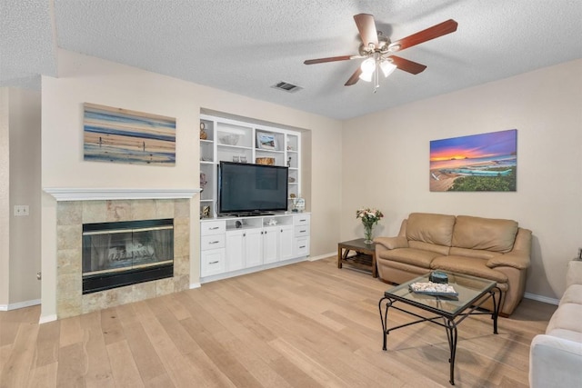 living area with a textured ceiling, visible vents, a ceiling fan, and light wood-type flooring