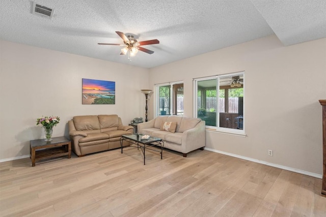 living room with a textured ceiling, ceiling fan, baseboards, and light wood-style floors