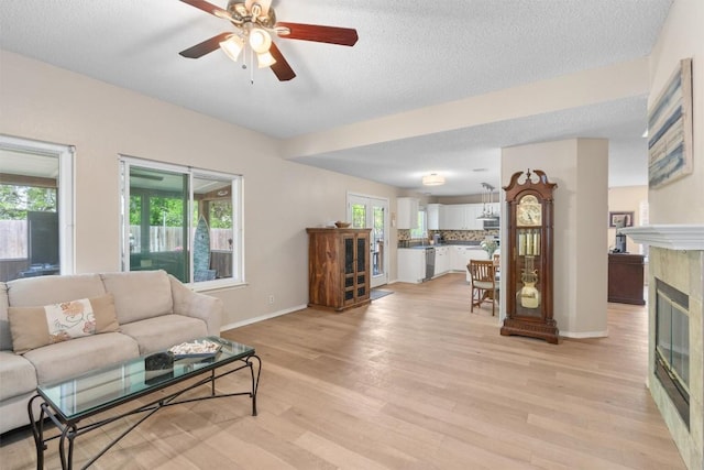 living area with a tile fireplace, a ceiling fan, light wood finished floors, and baseboards