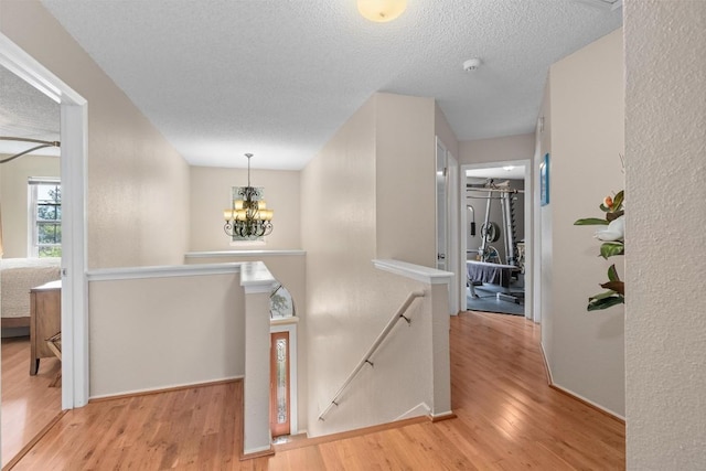 hallway with an upstairs landing, an inviting chandelier, wood finished floors, and baseboards