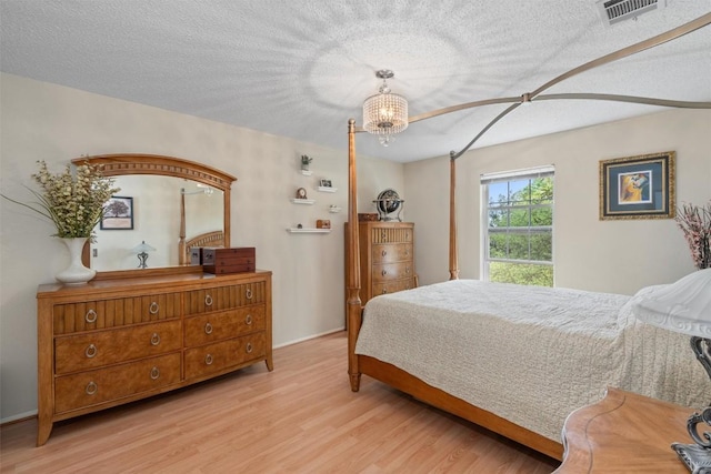 bedroom with wood finished floors, a chandelier, baseboards, visible vents, and a textured ceiling