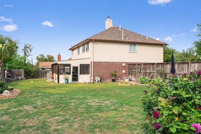 back of property with a fenced backyard, a chimney, a yard, brick siding, and a sunroom