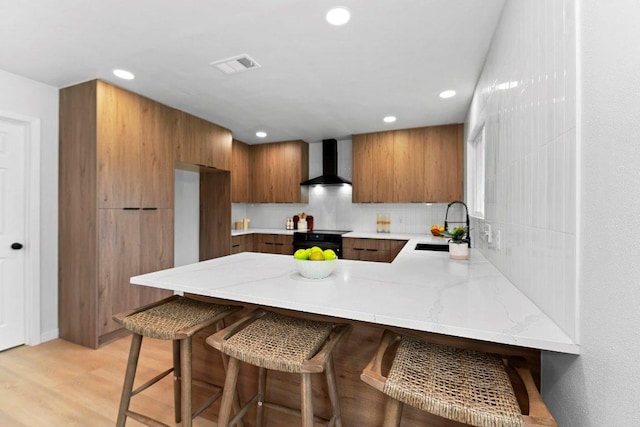 305 Pecan Ln, Round Rock, TX 78664 - kitchen featuring recessed lighting, wall chimney range hood, a sink, a peninsula, and brown cabinetry