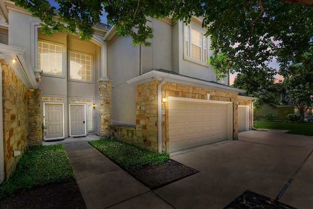 view of front facade featuring driveway, stucco siding, and stone siding