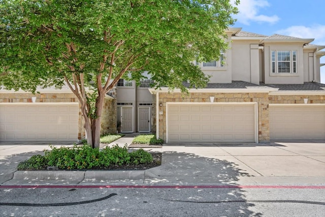 view of property with a garage, driveway, stucco siding, and stone siding