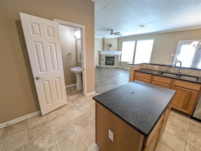 kitchen featuring brown cabinetry, a ceiling fan, a stone fireplace, a kitchen island, and a sink