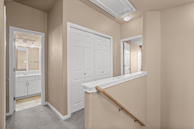hallway with light colored carpet, attic access, and baseboards
