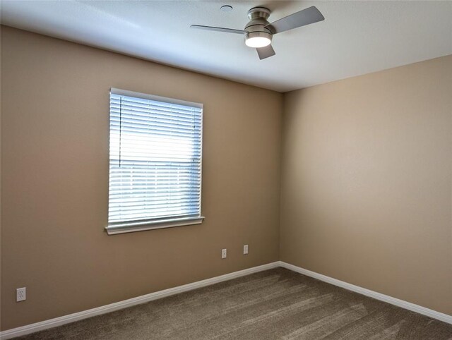 spare room with baseboards, dark carpet, and ceiling fan