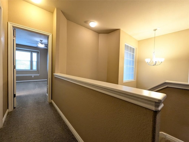 corridor with a chandelier, an upstairs landing, dark colored carpet, and baseboards