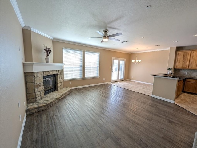 unfurnished living room with ornamental molding, a stone fireplace, baseboards, and ceiling fan with notable chandelier