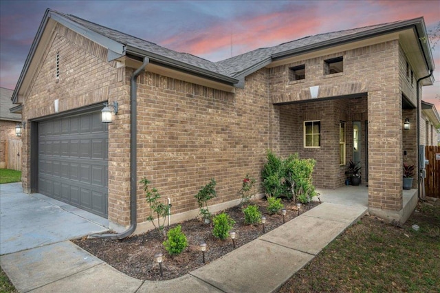 property exterior at dusk with concrete driveway, brick siding, roof with shingles, and a garage