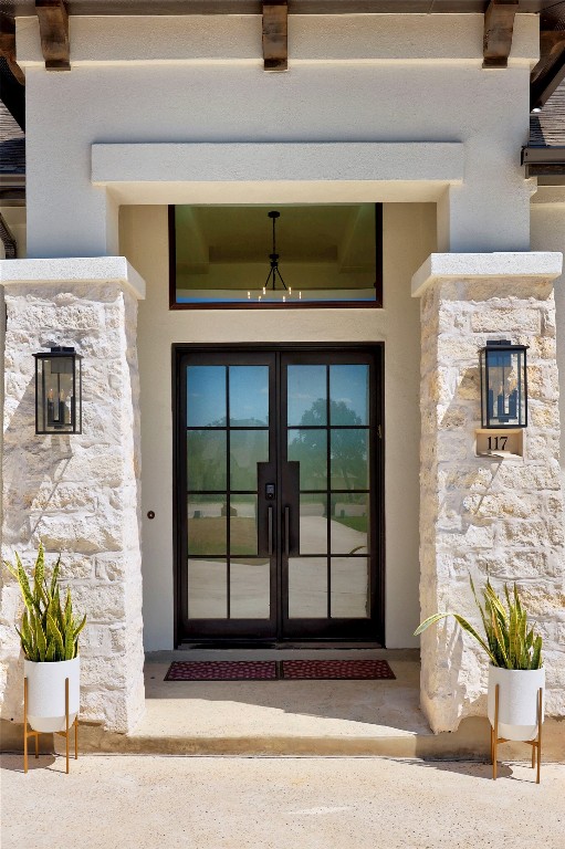 entrance to property featuring stone siding, french doors, and stucco siding