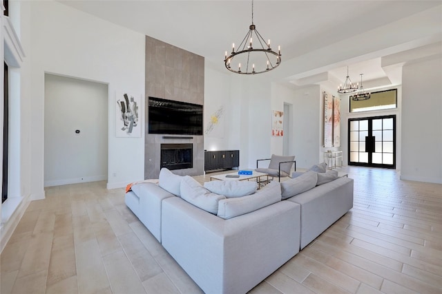 living area with baseboards, a towering ceiling, light wood-style flooring, a notable chandelier, and a tile fireplace