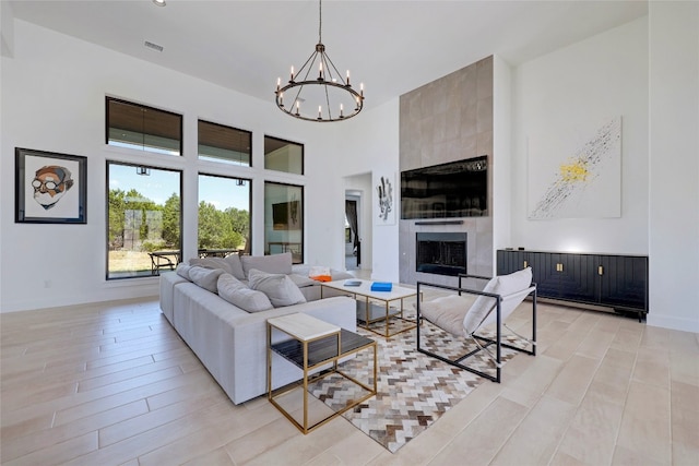living area with an inviting chandelier, a high ceiling, visible vents, light wood-style flooring, and a fireplace