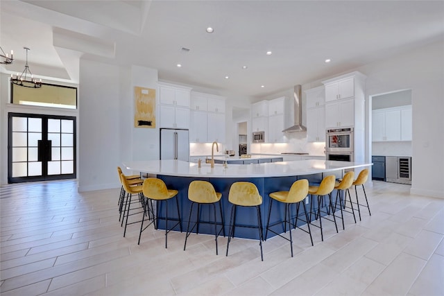 kitchen with a large island, wall chimney exhaust hood, white cabinets, and appliances with stainless steel finishes