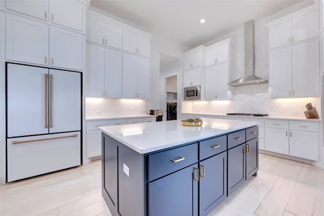 kitchen featuring white cabinetry, wall chimney range hood, high end fridge, and stainless steel microwave