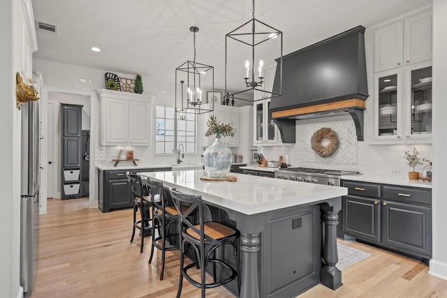 kitchen featuring a breakfast bar, light countertops, custom exhaust hood, and light wood finished floors